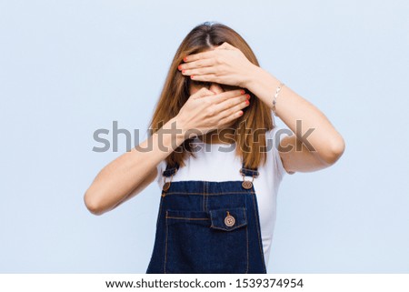 young pretty woman covering face with both hands saying no to the camera! refusing pictures or forbidding photos against blue background