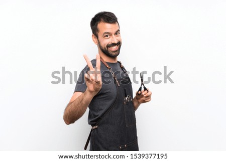 Barber man in an apron smiling and showing victory sign