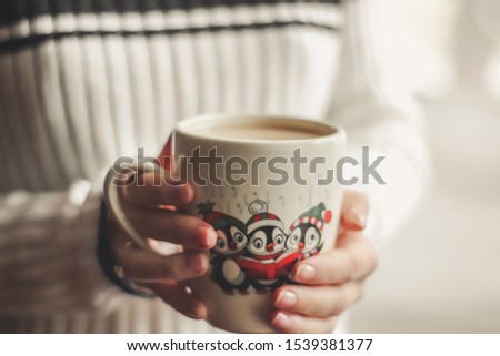 cup of coffee in female hands, cup with Christmas pattern, picture with penguins on cup, festive tableware, Christmas cup