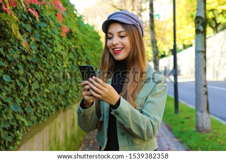 Portrait of beautiful young woman with hat messaging with smart phone on Autumn or Winter outdoors.