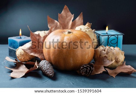 Pumpkin on dark background with candles and autumn leaves and pine cones.