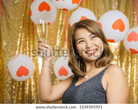 Happy Asian woman holding 
champagne glass with gold glitter background.