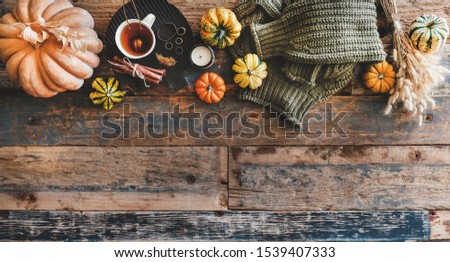 Autumn outfit layout. Flat-lay of dark green knitted sweater, blue jeans, hat, decorative pumpkins, candle, accessories and tea in cup on board over wooden background, top view, copy space Royalty-Free Stock Photo #1539407333