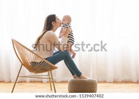 Sweet kiss. Mom holding her adorable little baby in hands and kissing his cheek