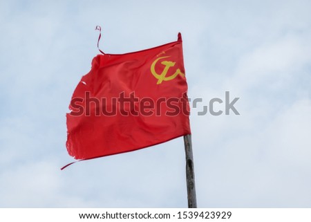Red soviet flag on sky background with clouds. The flag has a battered appearance. There is a sign of a sickle and a hammer. Background.