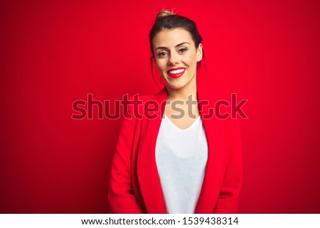 Young beautiful business woman standing over red isolated background with hands together and crossed fingers smiling relaxed and cheerful. Success and optimistic