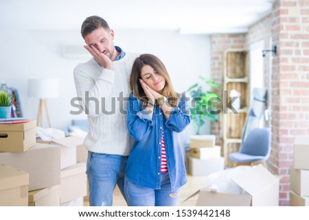 Young beautiful couple standing at new home around cardboard boxes sleeping tired dreaming and posing with hands together while smiling with closed eyes.