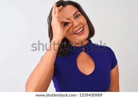 Young beautiful woman wearing blue elegant t-shirt standing over isolated white background with happy face smiling doing ok sign with hand on eye looking through fingers