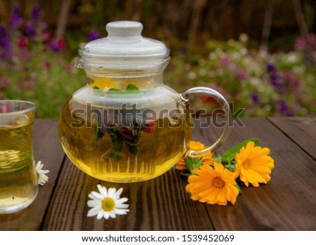 Transparent teapot and a Cup of herbal tea on a wooden table on a blurred background.Lay next to the calendula flowers.