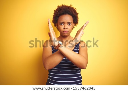 Beauitul african american woman wearing summer t-shirt over isolated yellow background Rejection expression crossing arms doing negative sign, angry face