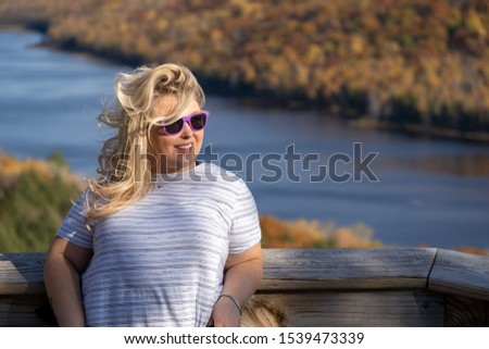 Adorable blonde woman poses at Lake of the Clouds in Porcupine Mountains wilderness state park in Michigan, looking away from camera