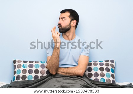 Man in bed with fingers crossing and wishing the best