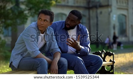 Black teenager male ignoring scolding dad sitting on campus bench, conflict Royalty-Free Stock Photo #1539525344