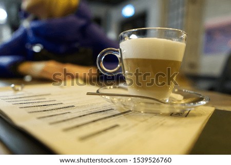 Glass mug with coffee latte in coffee on a vintage wooden table. Photo in dim light in warm colors on a wooden table with a menu under a coffee mug, lifestyle photo