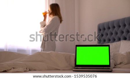 Laptop on bed, woman drinking juice relaxing near window, online travel booking