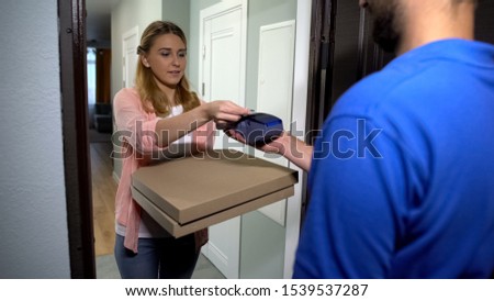 Woman taking pizza from delivery man, paying with bank card using terminal