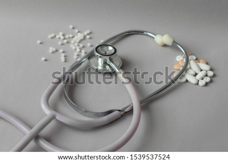 stethoscope between conventional medicines white and orange pills and natural medicines, homeopathic, white balls on gray background Royalty-Free Stock Photo #1539537524