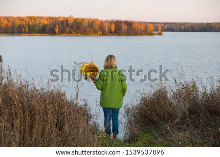 An adult woman walks along the shore of a forest lake, enjoying the autumn nature. Autumn. Active lifestyle of the elderly.
