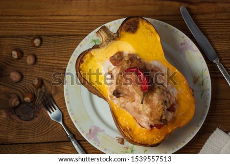 Stuffed pumpkin top view, flatlay. Halloween concept. Squash half with chicken breast, hazelnuts and red pepper on a wooden background. Spicy main dish, vegetables and meat.Food photography.Copy space