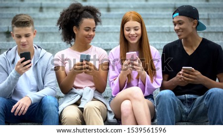 Happy multiethnic friends scrolling social networks app by smartphones outdoor