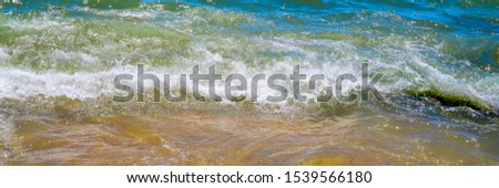 The wave rolls onto the sandy beach. Banner size picture.