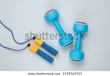 Minimalistic sport still life. Skipping rope and
dumbbells on white background. Top view