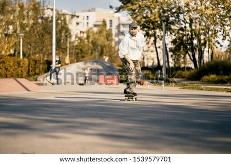 Man with beard in skatepark rides skateboard on warm autumn day