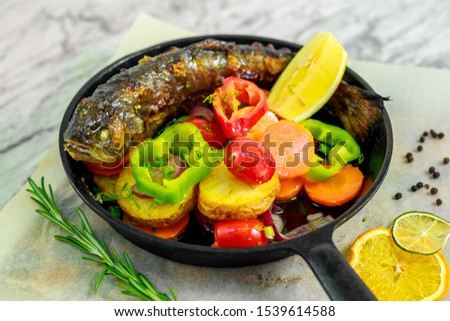fried fish in a pan with rosemary and vegetables