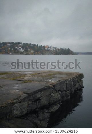 Scandinavian landscape. Lonely stone berth. Nobody. Background for people. Autumn in Sweden. Stockholm archipelago.  Foggy wet weather. Baltic sea in fall season. Vertical Instagram photo.