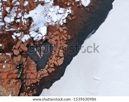 DRONE, TOP DOWN: Two tourists look up into the sky while sitting in a hot spring in snowy Colorado. Flying above young couple travelling across the United States while relaxing in Radium hot springs. Royalty-Free Stock Photo #1539630986