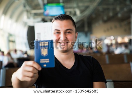 Young travel man waiting for plane in airport while holding ukrainian passport in hands.