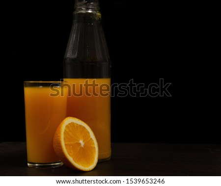 Glass of juice and orange on black background