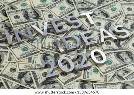 The words INVEST IDEAS 2020 with metal letters on the US dollar bills background - with selective focus