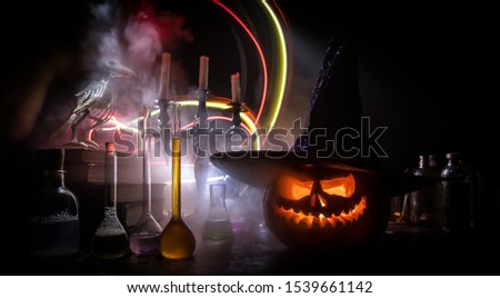 Wizard's Desk. Horror Halloween concept. Magic potions in bottles on wooden table with books and candles. Halloween still-life background with different elements on dark toned foggy background. 