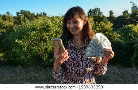 Young girl with dark hair showing money banknotes in her hands and using mobile. The concept of business and entrepreneurship. 