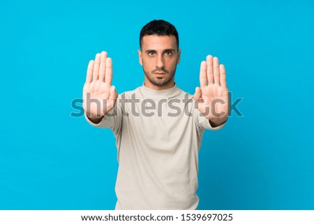 Young man over isolated blue background making stop gesture and disappointed