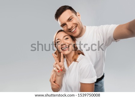 relationships, technology and people concept - happy couple in white t-shirts taking selfie smartphone and showing peace by over grey background