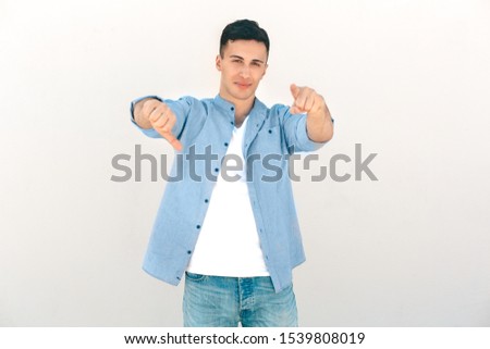 Stylish young man standing outdoors isolated on white background pointing at camera showing thumb down dislike smiling cool