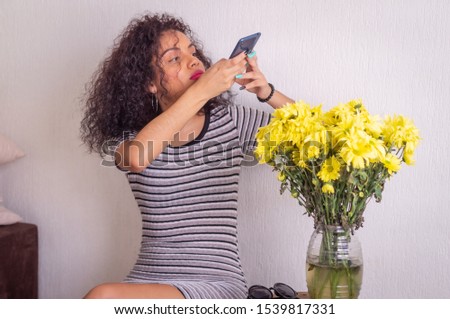 Young pretty woman photographing with her cell phone bouquet of yellow flowers.
