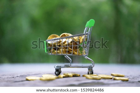 Gold coins in shopping cart closeup on wooden table blur green nature background