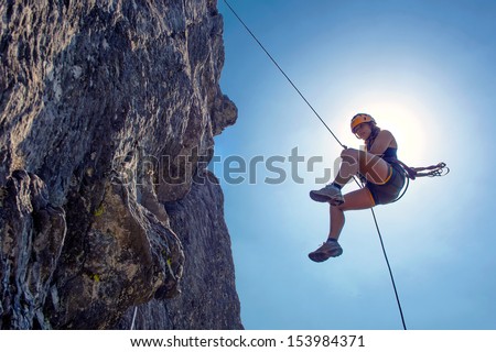 Young, tough, woman, abseiling from a steep rock, just in front of the sun Royalty-Free Stock Photo #153984371