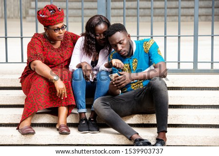 beautiful happy family, young man showing a pictures, information on cell phone has his mother and sister sitting on the stairs near him on the street smiling