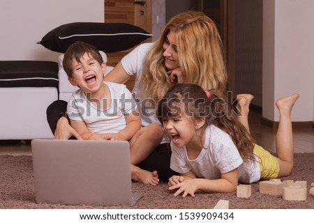 Happy mom on the floor at home with kids and watch funny cartoon on laptop.
