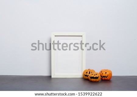 Mock up black frame with Jack o Lantern and pumpkin decor on a shelf or desk. 2020 Halloween concept. Portrait frame against a white wall, cop