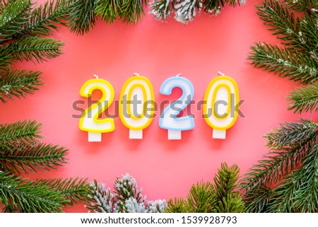 2020 New Year design. Date laid out by candles near fir branches on pink background top view