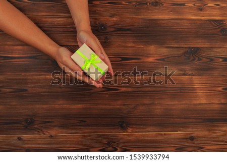 gift in female hands on a wooden background top view.