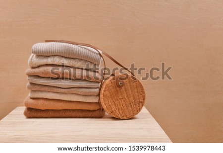 Knitted wool sweaters. Pile of knitted winter clothes with round bamboo handbag on wooden background


