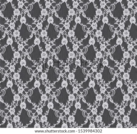 Seamless pattern in the form of white lace on a black background. Flower ornament. Tulle. Detailed texture of lace.