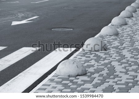 White pedestrian crossing on an asphalt road in the middle of a modern city, next to a sidewalk made of gray stone and concrete stoppers