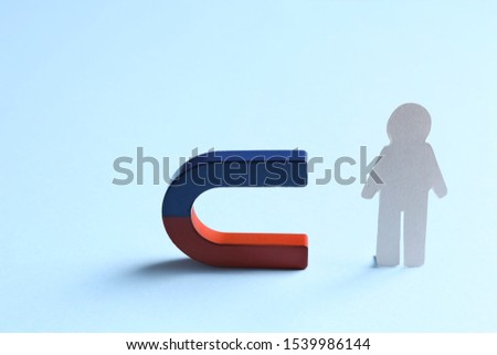 Magnet attracting paper person on light blue background